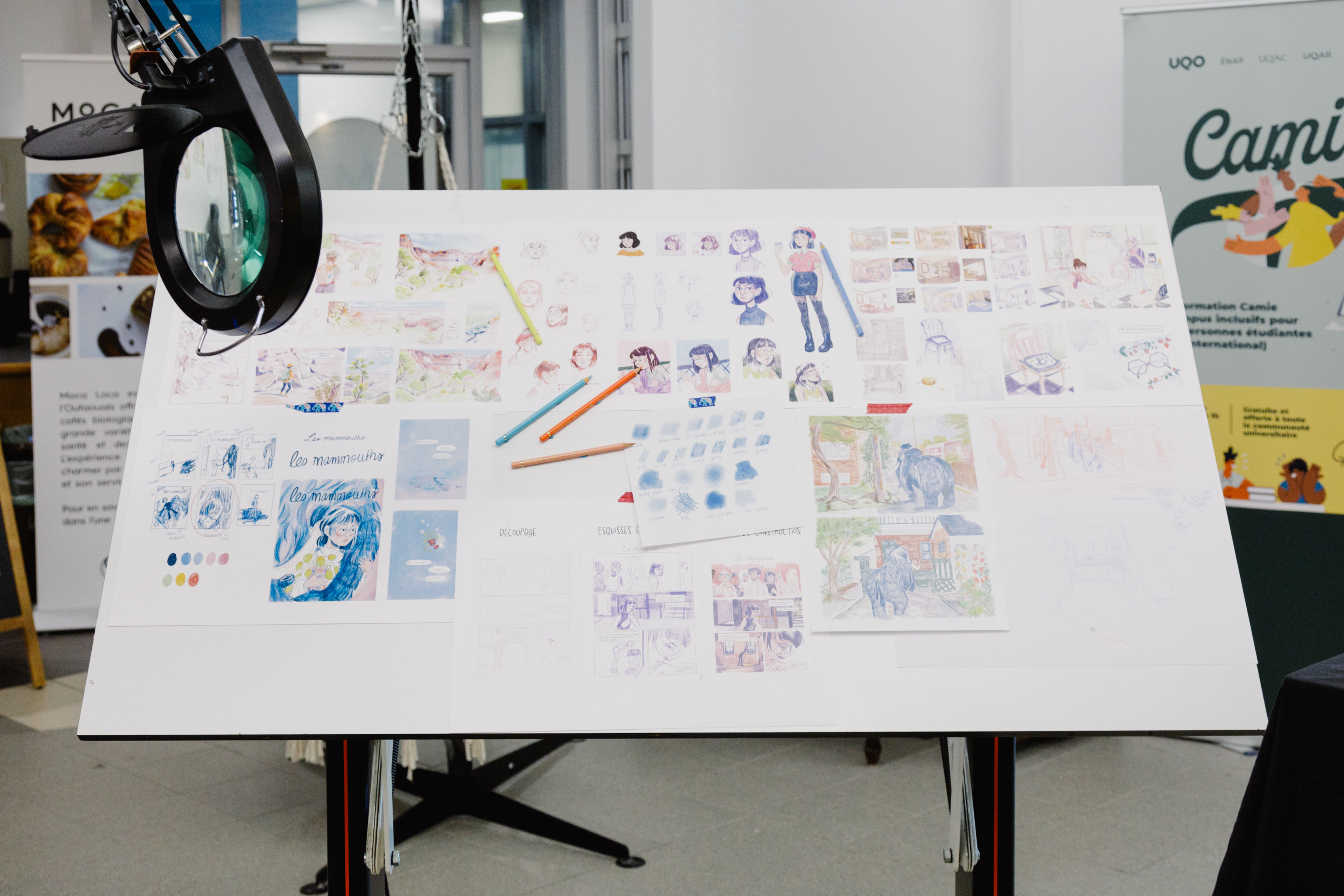 Des planches de bande dessinée sont disposées sur une table à dessin dans le cadre d'une exposition de l'ÉdAC.