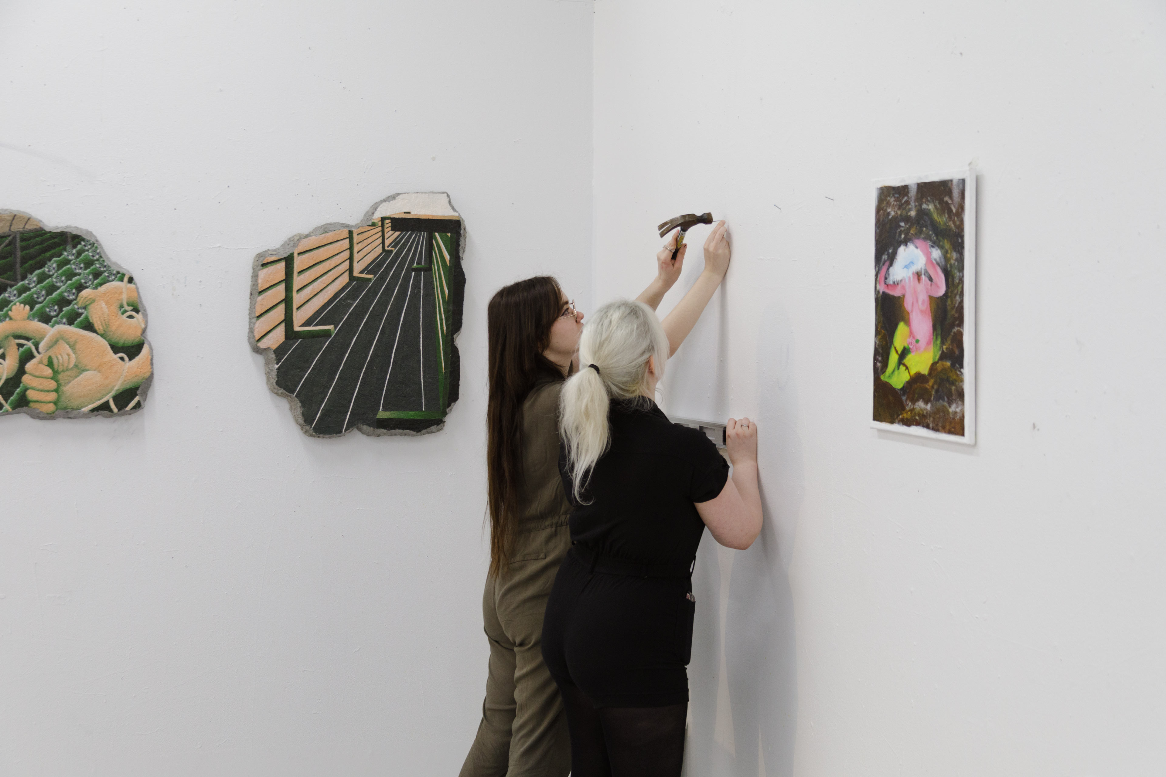 Deux étudiantes accrochent leurs œuvres au mur pour une exposition de fin d'année à l'ÉdAC.