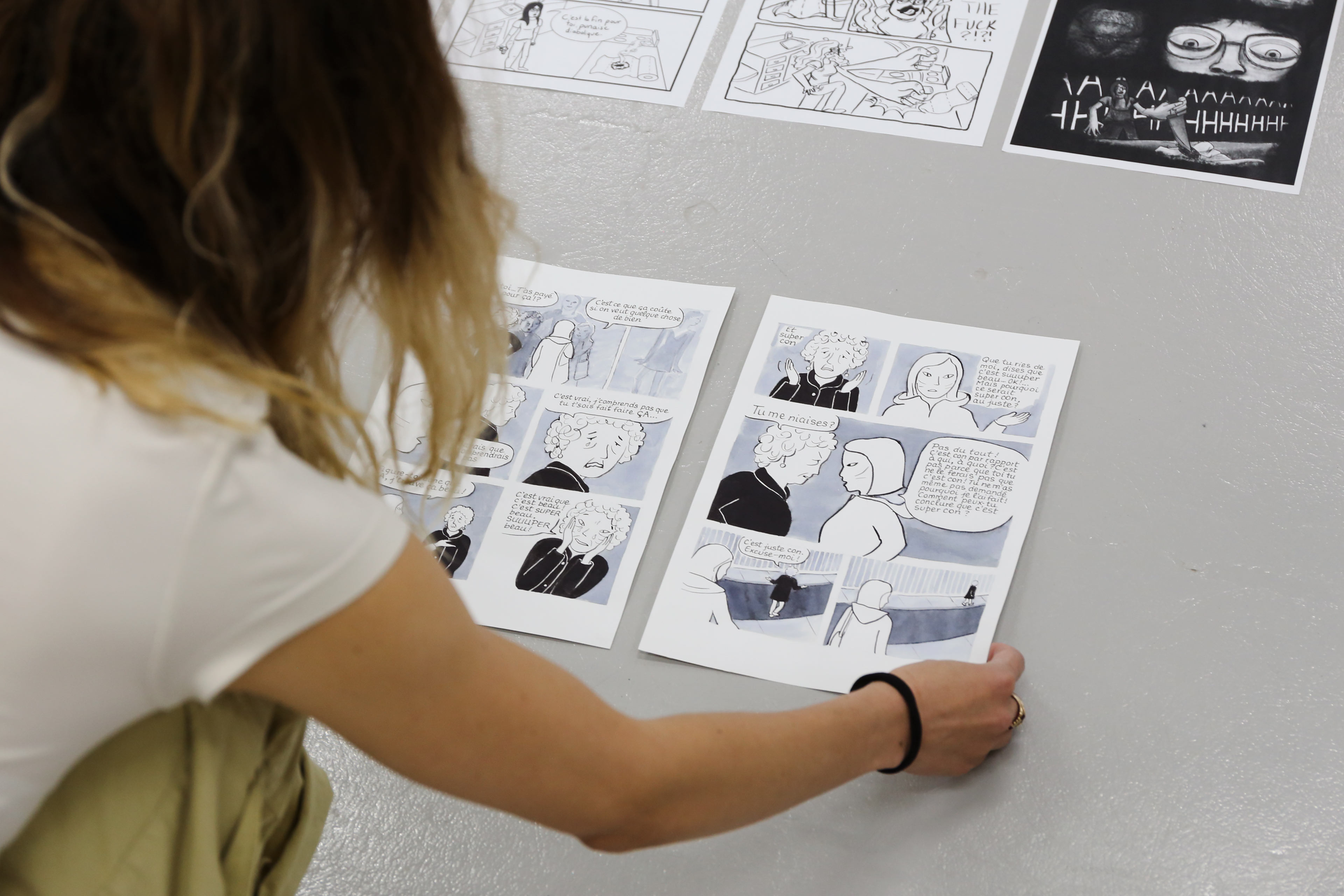 Une personne dispose des planches de bande dessinée au sol pour une exposition de fin d'année à l'ÉdAC.